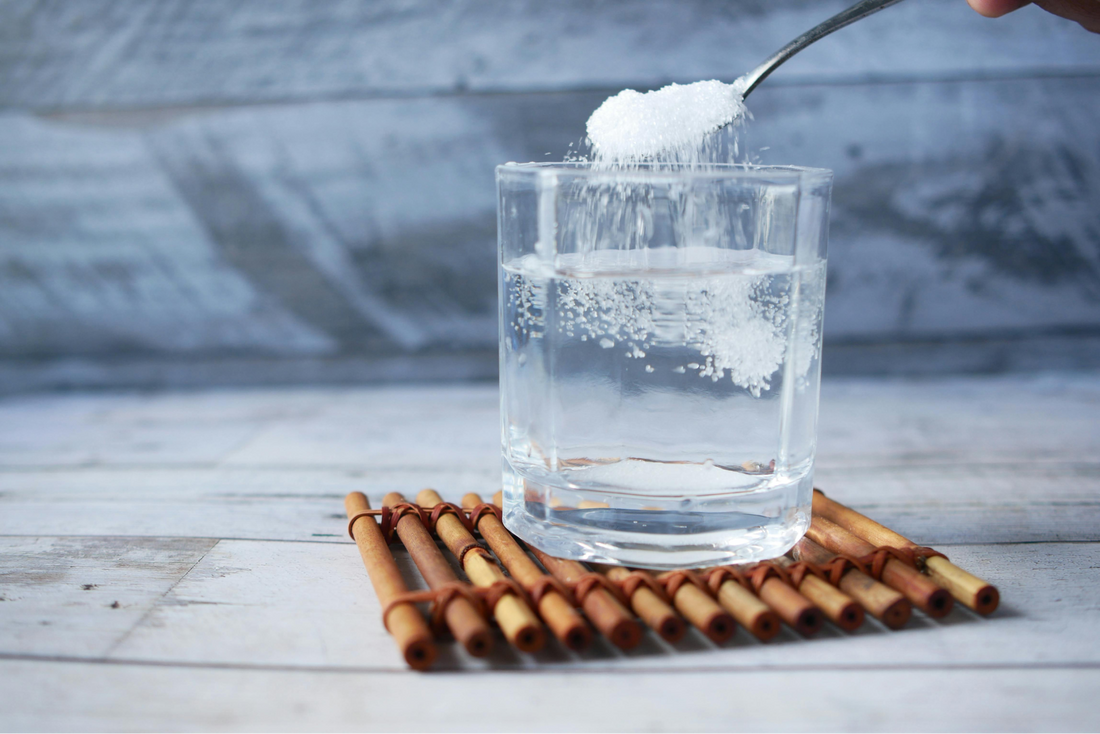 water cup on coaster with collagen powder going into the water